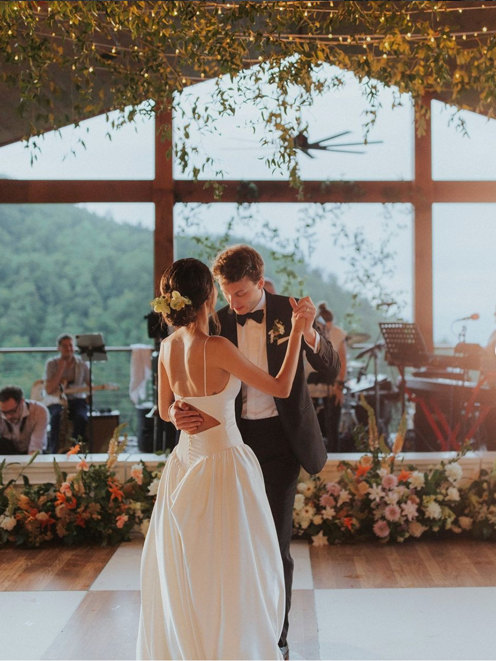 Couple dancing at a wedding with a scenic background, dance floor, band and string lights